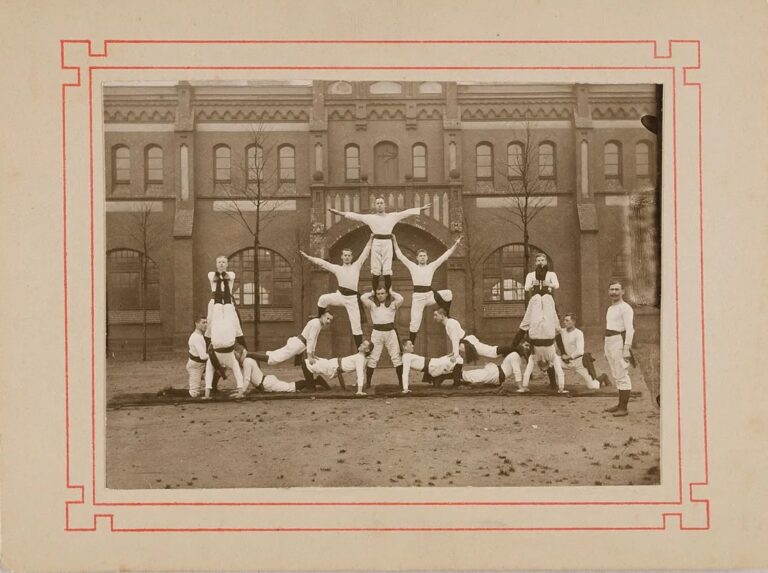 Black and white photograph of men in twentieth-century white sporting outfits standing in acrobatic formation