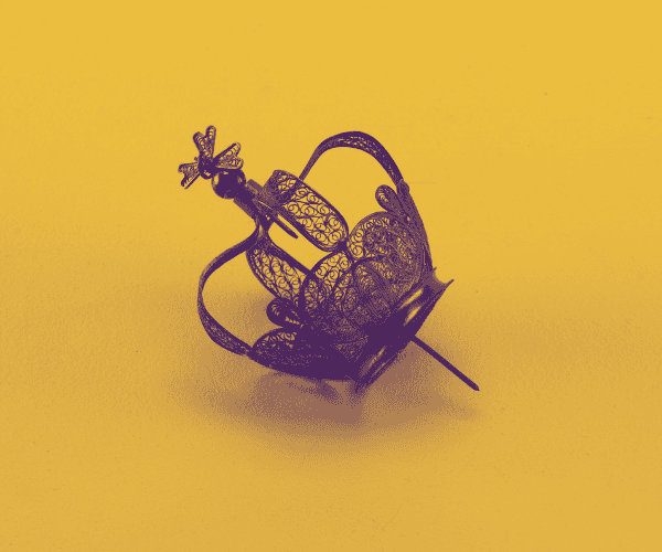 Silver filigree pin of a crown against yellow background. Four kidney-shaped panels, pierced with filigree work, rising from a plain diadem. From the panels rise four curved arches, meeting to support a ball and a cross mounted on a threaded pin.